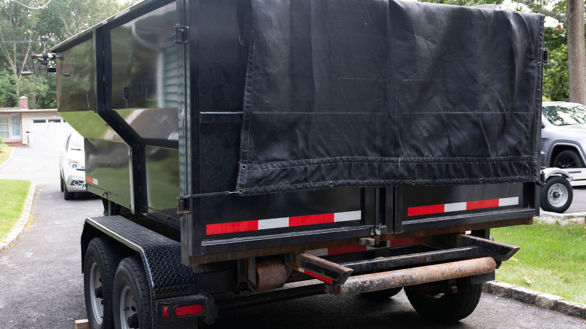 Black covered trailer with red safety stripes parked on residential street