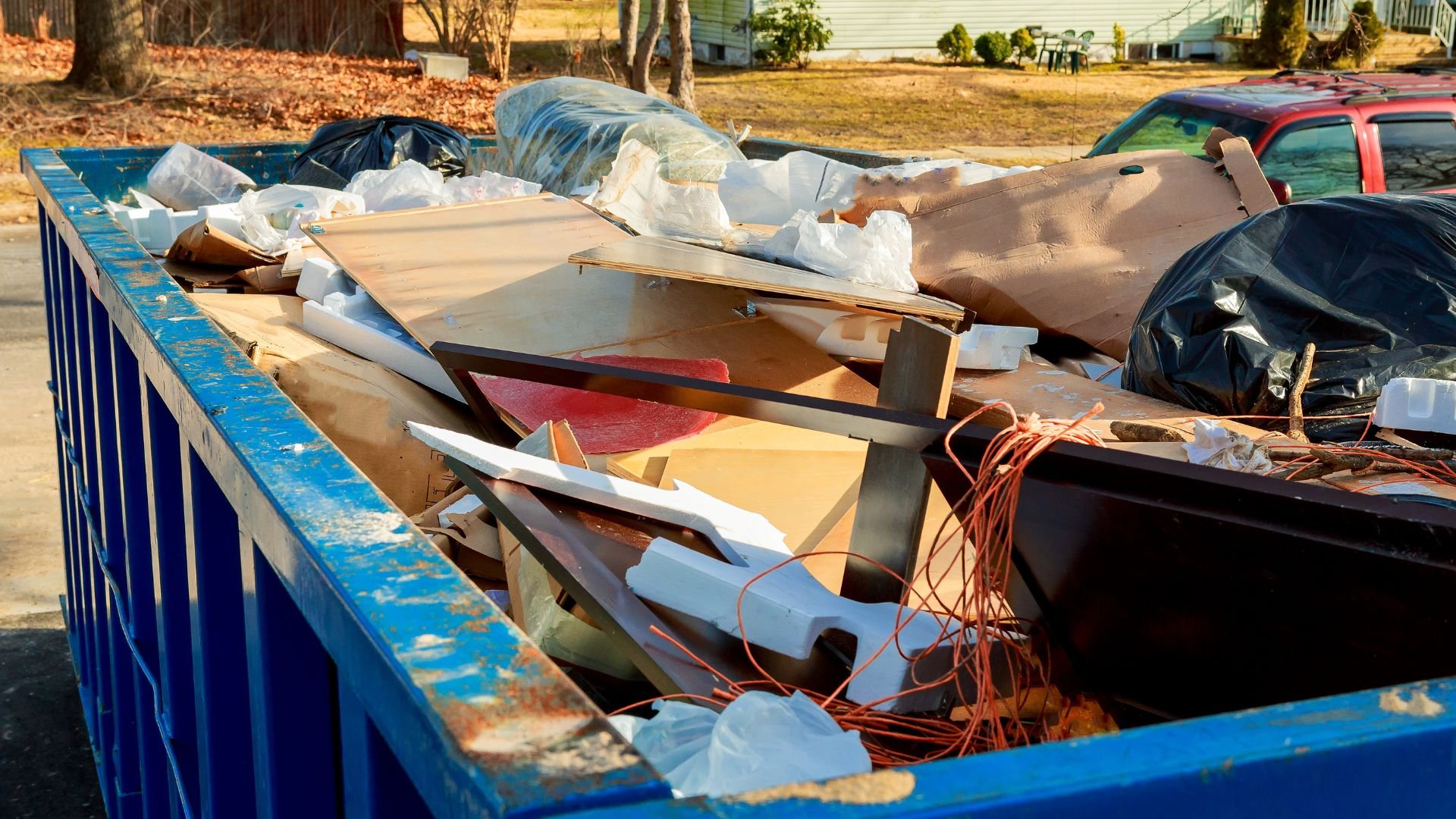 Blue dumpster filled with construction debris, wood, and trash bags