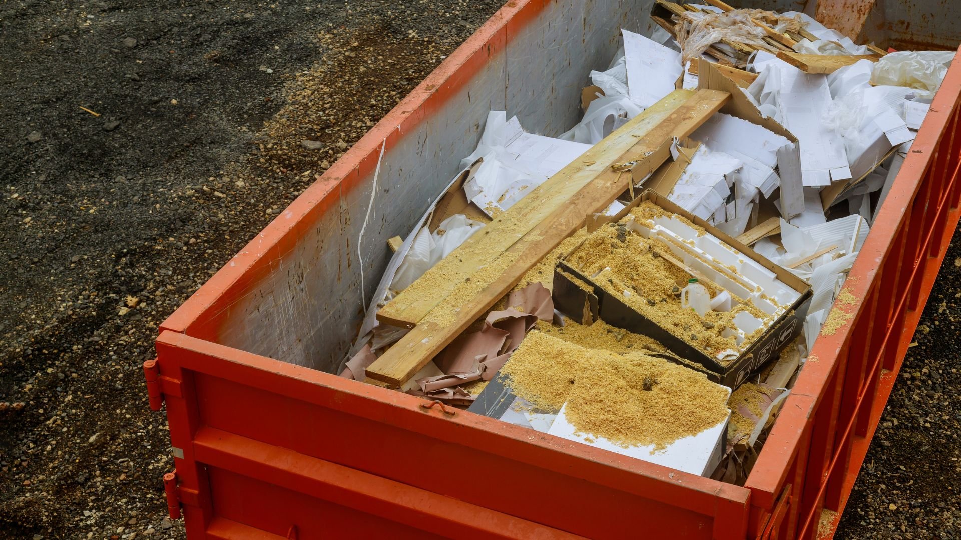 Red construction dumpster filled with wood, sawdust, and construction debris