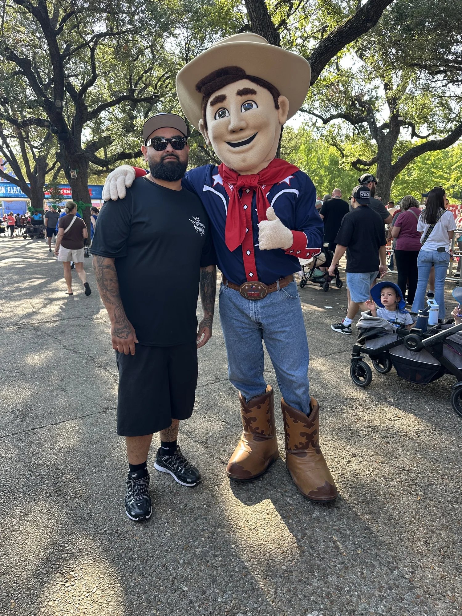 Mascot and person standing together at outdoor event under trees