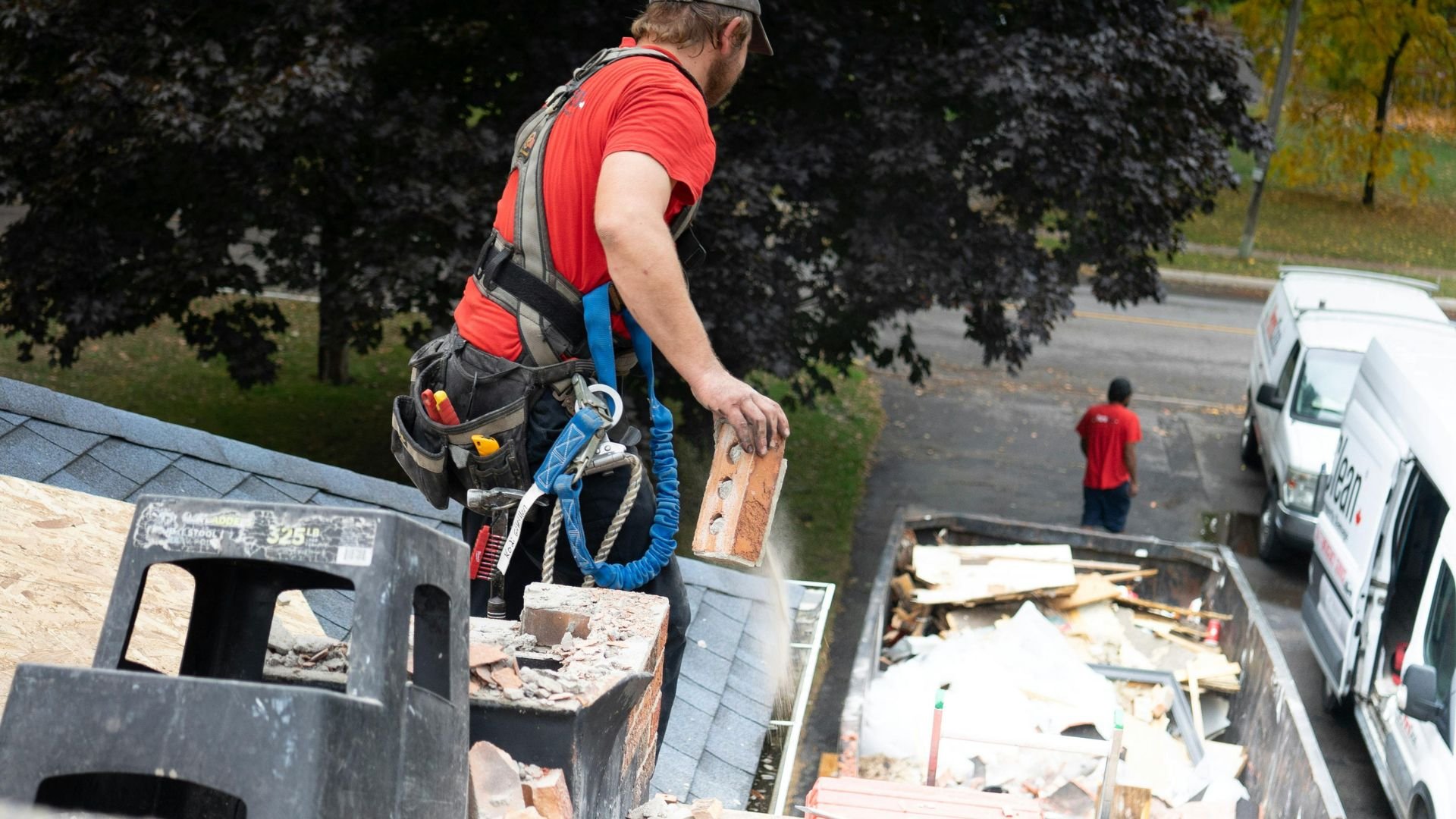 Roofer in red shirt working on roof with safety harness and tools