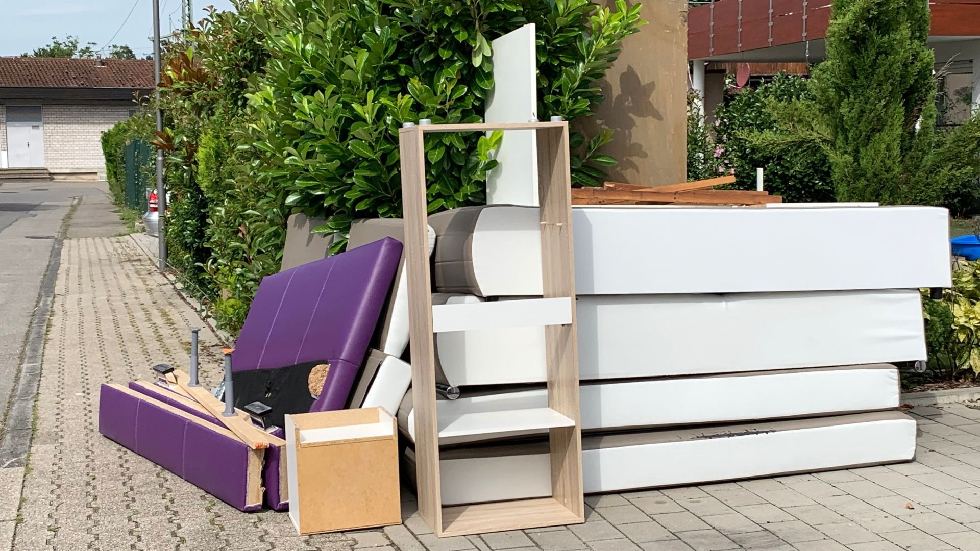 Discarded furniture, purple chairs, white drawers, and wooden shelving outside