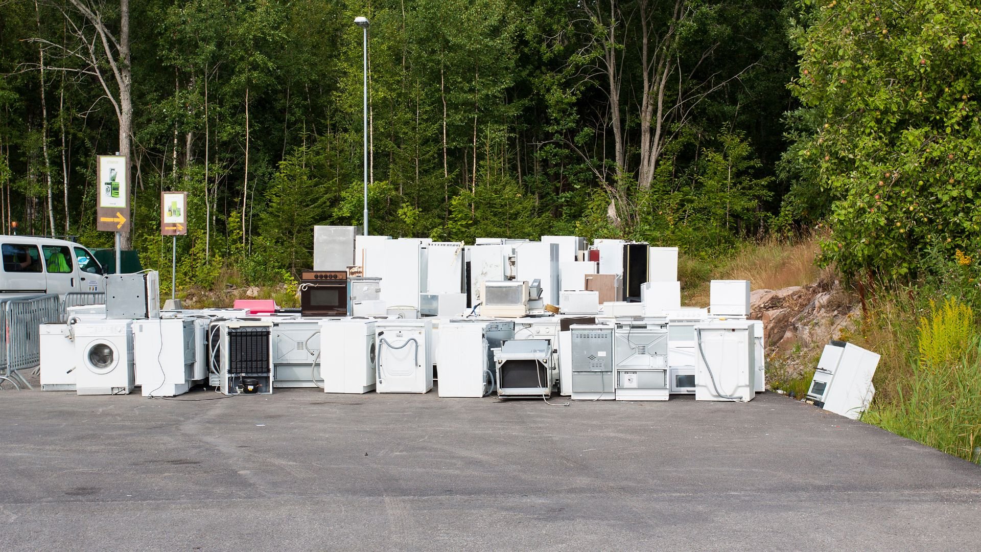 Pile of discarded white household appliances at recycling center near forest