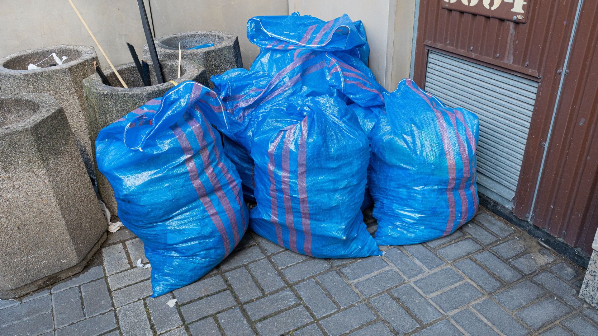 Blue and pink striped garbage bags stacked on brick pavement near wall